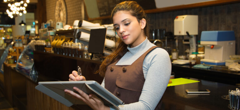 Portrait of confident young female cafe owner wearing uniform writing in register book or menu