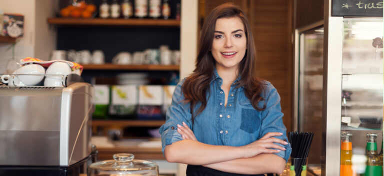 Portrait of confident young female cafe owner wearing uniform writing in register book or menu